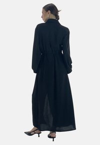 Zwarte jurk met lange mouwen en een kraag, cinched taille en volle rok; gemaakt van een lichtgewicht, iets doorschijnende stof.