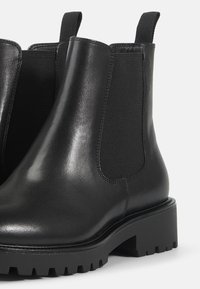 Črne usnjene Chelsea čizme z elastiko na straneh, okroglo konico in debelim, teksturiranim gumijastim podplatom. Tablaje za lažje obuvanje na gležnju.