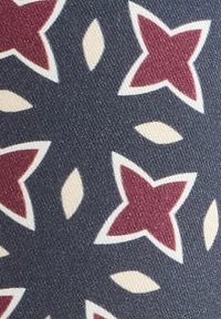 Tmavě modrá tkanina se tvarovými hvězdami v maroon a bílé barvě a bílými oválnými listovými vzory v opakujícím se designu.
