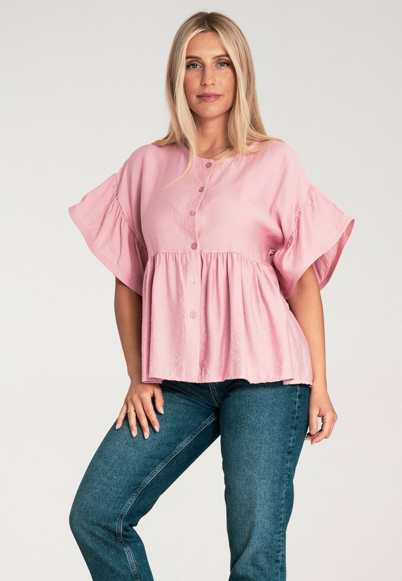 Różowa bluzka z krótkim rękawem, zapinana na guziki, z marszczoną talią; materiał wydaje się lekki o miękkim, lekko teksturowanym wykończeniu. Luźny krój.