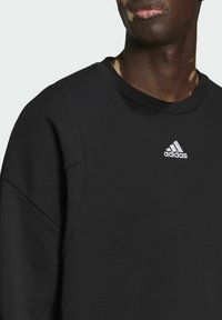 Felpa nera con collo a girocollo a coste, caratterizzata da un piccolo logo bianco Adidas sul petto. Le maniche hanno una vestibilità comoda e una finitura pulita.