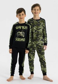 Dvaja chlapci majú na sebe rovnaké pyžamá: jedno čierne s textom "GAMER SQUAD" a grafikou herného ovládača, druhé v zelenom maskáčovom vzore.