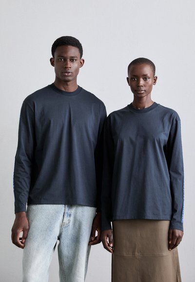 Marineblaue langärmlige T-Shirts aus einem weichen Stoff, mit Rundhalsausschnitten und geraden Säumen, kombiniert mit heller Jeans und einem braunen Rock.