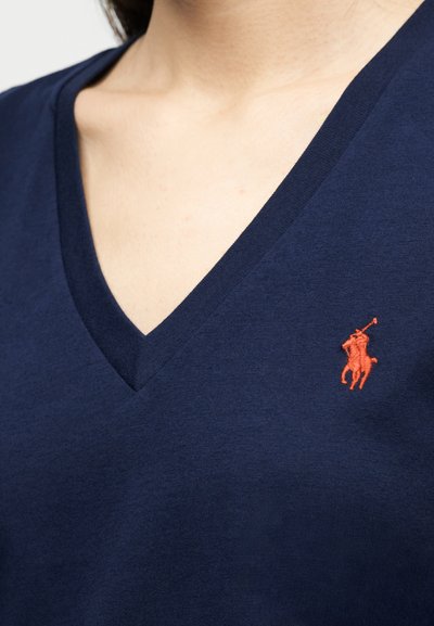 Κοντινή λήψη μπλε-ναυτικού V-neck πουκάμισου με μικρό κόκκινο κεντητό λογότυπο πόλο παίκτη στο στήθος.