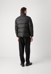 Svart dunjakke med horisontalt quiltet design, høy krage og elastiske mansjetter, paret med svarte cargo-bukser og flate sko.