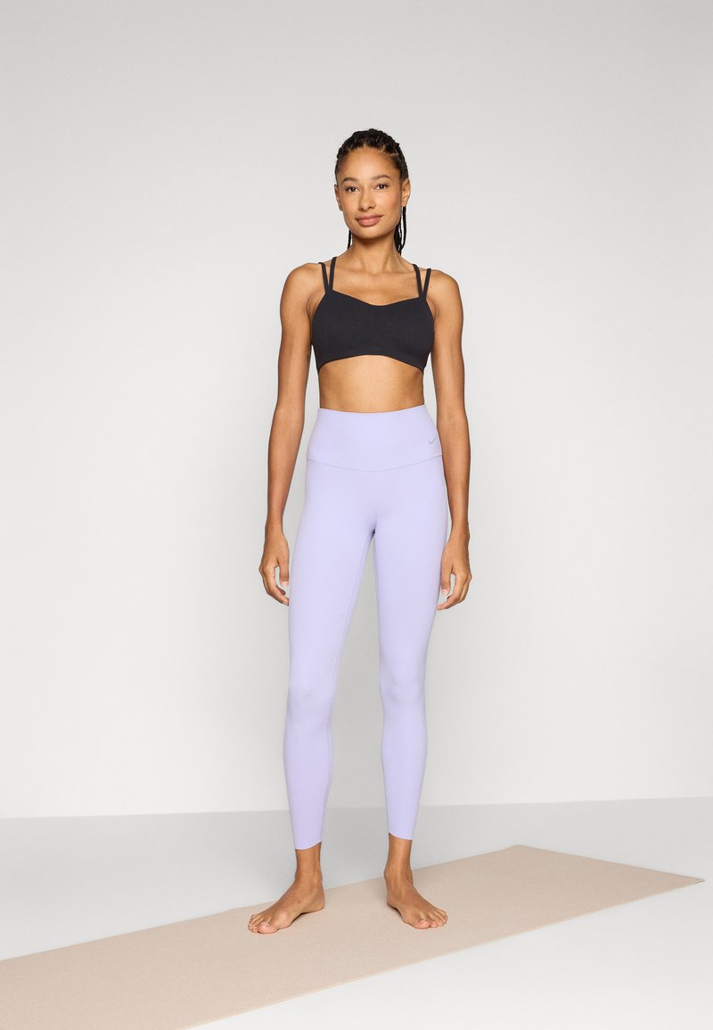Czarny stanik sportowy i jasnolawendowe legginsy, oba dopasowane, o gładkiej fakturze. Stanik ma cienkie ramiączka i minimalistyczny design.