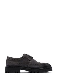 Chaussures brogue en daim gris foncé avec des détails perforés et une semelle en caoutchouc noir robuste, présentant un bout arrondi et un laçage.