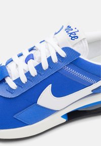 Chaussette de sport bleue avec une tige en toile texturée, des lacets blancs et un logo swoosh blanc. Présente des accents superposés et une semelle rembourrée.