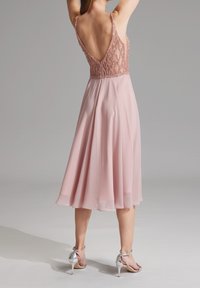 Sukienka do kolan w miękkim różowym szyfonie, z koronkowym gorsetem zdobionym koralikami, odkrytymi plecami i delikatnymi ramiączkami spaghetti. Połączona z srebrnymi szpilkami.