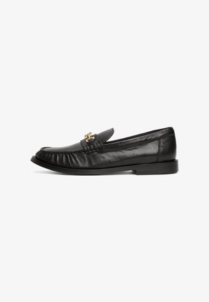 Black leather loafer with a rounded toe, decorative gold hardware, textured stitching on the vamp, and a low flat sole.