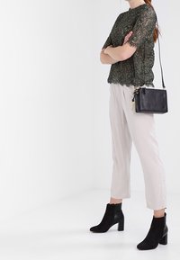 Zielony top z koronką i krótkimi rękawami, jasne spodnie oraz czarne botki za kostkę. Do zestawu dołączona jest mała czarna torebka z złotym akcentem.