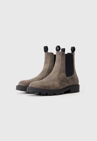 Een paar bruine leren Chelsea-boots met zwarte elastische zijpanelen en robuuste zwarte zolen op een effen witte achtergrond.