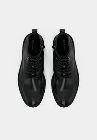 Črni usnjeni gležnarji z gladkim zaključkom, z zavezovanjem na vezalke, kovinskimi poudarki in trdnim gumijastim podplatom.