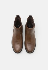 Botas de tobillo de cuero marrón con paneles laterales elásticos, punta redondeada y suela de goma negra. Textura suave con detalles de costura mínimos.