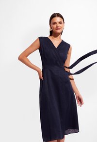 Granatowa sukienka kopertowa z lnu, z dekoltem w serek, bez rękawów, z fakturowanym wykończeniem wzdłuż korpusu i wiązaniem w talii.