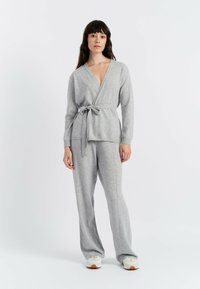 Grijze gebreide wikkeltop met strik taille, lange mouwen en diepe V-hals. Combinatie met bijpassende brede broek, met subtiele stikdetails.