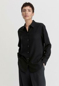 Schwarz, langärmliges Hemd mit Knopfleiste und Kragen, aus einem glatten Material gefertigt. Verfügt über eine lockere Passform und ein minimalistisches Design.