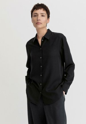 Schwarz, langärmliges Hemd mit Knopfleiste und Kragen, aus einem glatten Material gefertigt. Verfügt über eine lockere Passform und ein minimalistisches Design.