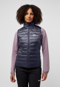 Gilet matelassé bleu marine avec un col haut, doté d'un zip à l'avant et d'un design matelassé. Associé à des manches longues texturées violet clair.