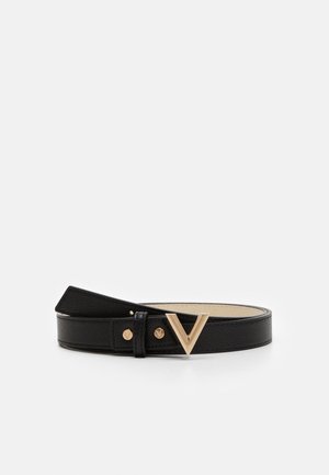 Ceinture en cuir noir texturé avec boucle dorée en forme de V et deux clous dorés, enroulée sur un fond blanc.
