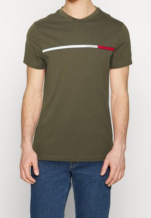 Mand iført en olivengrøn kortærmet t-shirt med horisontale hvide og røde striber og "Tommy Hilfiger" logo, kombineret med blå jeans.