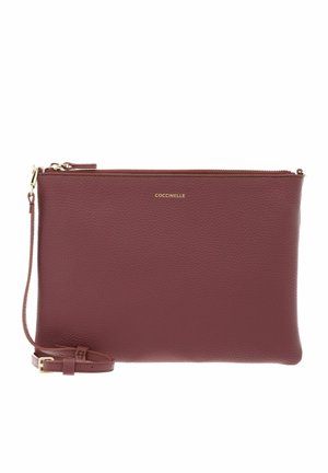 Pochette poignet rectangulaire en cuir bordeaux avec fermeture éclair dorée et petit nom de marque doré sur le devant, sangle amovible avec boucle.