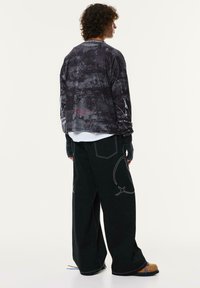 Črn dolgrokavnik s teksturiranim vzorcem, v kombinaciji z ohlapnimi temnimi hlačami z kontrastnim šivanjem in edinstvenimi detajli na robu.