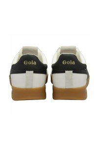 Witte en zwarte Gola sneakers met een gumrubberen zool, voorzien van een suède hielstuk, textuurleer en goudkleurig logo detail op de achterkant.
