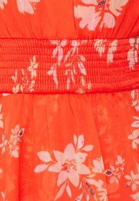 Robe florale avec un corsage smocké, en tissu orange léger, de grands motifs floraux blancs et une texture de jupe fluide.