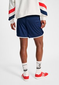Marinafärgade sportshorts med vit kant, i kombination med röda sneakers och svarta strumpor med ränder, mot en enkel vit bakgrund.