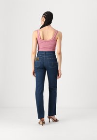 Denim jeans in dark blue with a high waist, two back pockets, and a branded patch. Paired with a light pink ribbed tank top.