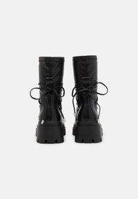 Botas de tobillo negras de cuero suave, con suela gruesa, punta redondeada y diseño de cordones con bucles de tela en la parte posterior.