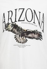 White cotton t-shirt featuring a graphic of an eagle with outstretched wings, "ARIZONA" text above, and "PHOENIX MOTOR CLUB" below.