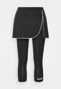 Svart idrottskjol med vit kant, lagerdesign, kombinerad med svarta leggings. Materialet har en slät, elastisk textur.