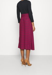 Midiklänning i rosa houndstooth-mönster, kombinerad med en svart långärmad topp och beige högklackade skor. Slät tygstruktur.