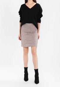 Un pull noir ample à col en V associé à une jupe moulante côtelée de longueur genou avec un motif rose et gris moucheté, portée avec des bottines noires.