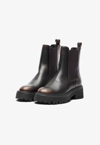 Botas de cuero marrón hasta el tobillo con inserciones elásticas en los laterales y lengüetas. Suelas de goma negra gruesa con un patrón de tracción robusto. Acabado suave y punta redondeada.