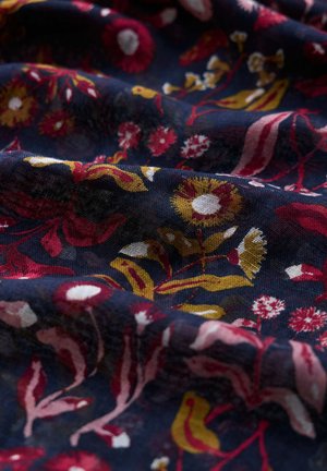 Donkerblauwe stof met getextureerde plooien, versierd met een bloemmotief van rode, gele en witte bloemen en bladeren.