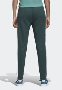 Green sweatpants with white side stripes, fitted design, and soft texture, paired with blue sneakers featuring white accents.