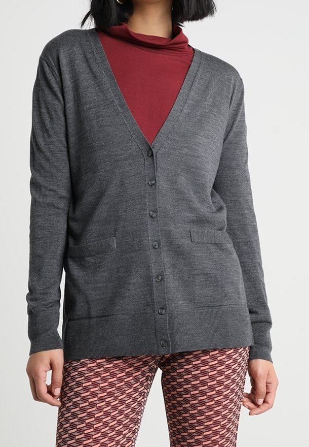 Grå cardigan med V-ringning, knäppning framtill och två framfickor. Buren över en vinröd polotröja och mönstrade röda leggings.