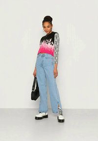 Top sem mangas multicolorido com gradiente rosa e mangas longas às riscas de zebra, combinado com umas calças azuis claras e sapatos brancos de plataforma. Bolsa preta.