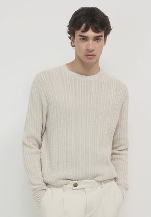 Maglione beige lavorato a maglia con righe verticali, scollo tondo, maniche lunghe e una vestibilità comoda, abbinato a pantaloni crema.