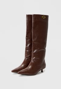 Bottes hautes marron en faux cuir avec une texture crocodile, bouts pointus et petits talons. Comprend un accent en diamant noir et or.