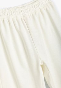 Kremowe dresy z elastycznym pasem i gładką, miękką fakturą materiału. Posiadają kieszeń w bocznym szwie.