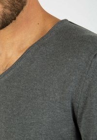 Grå V-hals sweater lavet af blødt stof, med en finstrikket tekstur og en standard pasform, der fremhæver halsudskæringen og skuldersømmen.