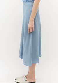 Jupe midi fluide bleu clair en tissu doux, avec un ourlet asymétrique et une fermeture éclair discrète sur le côté.