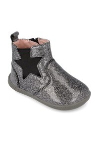 Botín metálico brillante con un panel elástico negro y un corte en forma de estrella. Punta redondeada y suela de goma gris. Forro interior rosa claro.