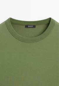 Olijfgroene T-shirt met korte mouwen en een geribde ronde hals. Voorzien van een zwart label met de tekst "Massimo Dutti, Made in Portugal." Soepele textuur.