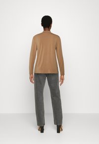 Top de manga longa castanho, design ajustado, tecido leve. Combinado com jeans cinza soltos e sandálias de salto bloco pretas.