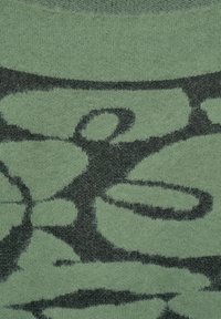 Dzianina o miękkiej fakturze, z zielonym tłem i wyraźnymi czarnymi, abstrakcyjnymi wzorami, podkreślającymi jej unikalny design i kontrast kolorów.